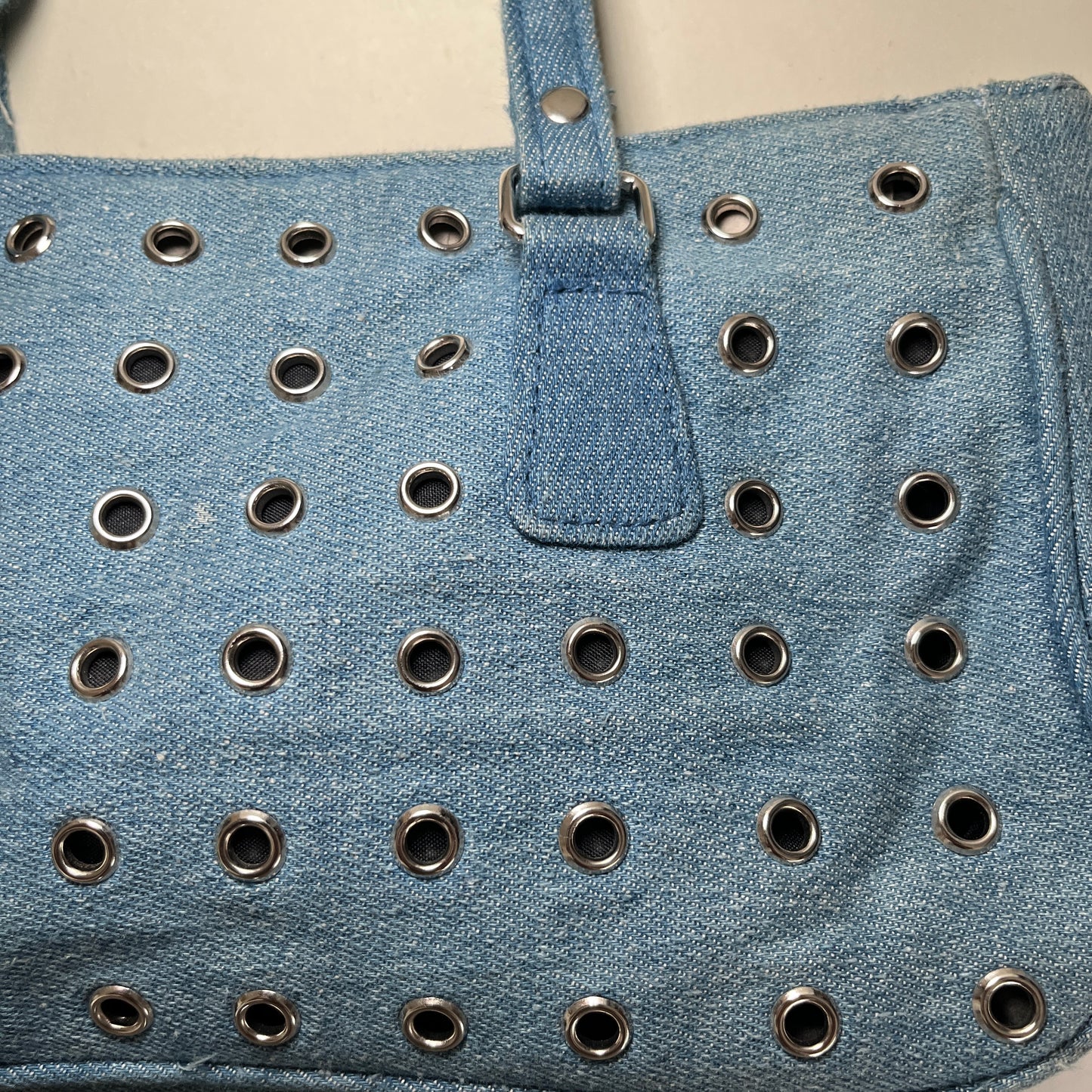 Sac baguette en denim à oeillets métalliques.